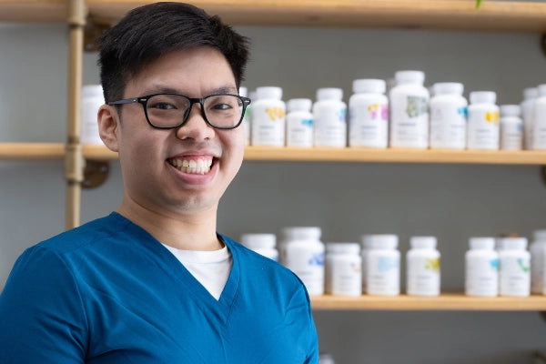 Smiling Quinn's Apothecary Pharmacy male staff member in front of wall of wellness products