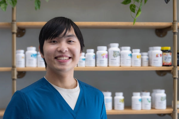 Smiling Quinn's Apothecary Pharmacy male staff member in front of wall of wellness products