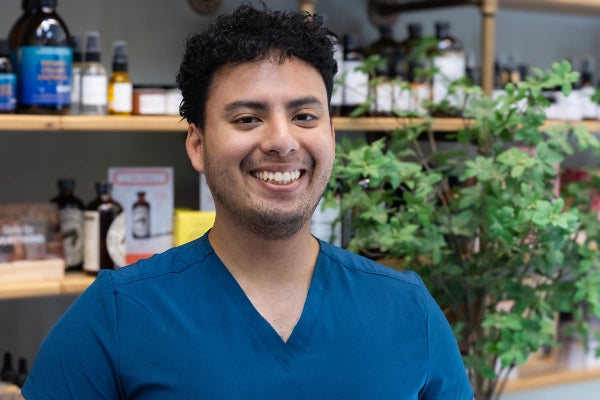 Smiling Quinn's Apothecary Pharmacy male staff member in front of wall of wellness products