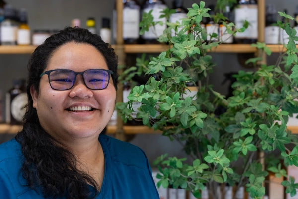 Smiling female pharmacist staff member at Quinn's Apothecary Pharmacy in front of wall of wellness products