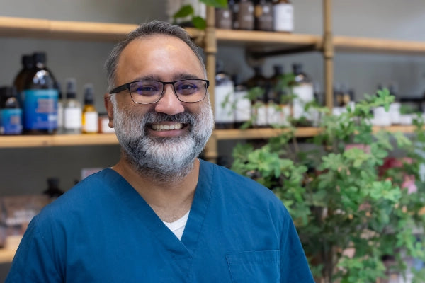 Smiling Quinn's Apothecary Pharmacy staff member in front of wall of wellness products