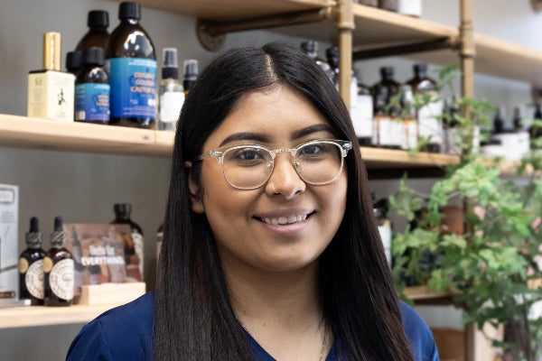 Smiling pharmacist female staff member at Quinn's Apothecary Pharmacy in front of wall of wellness products